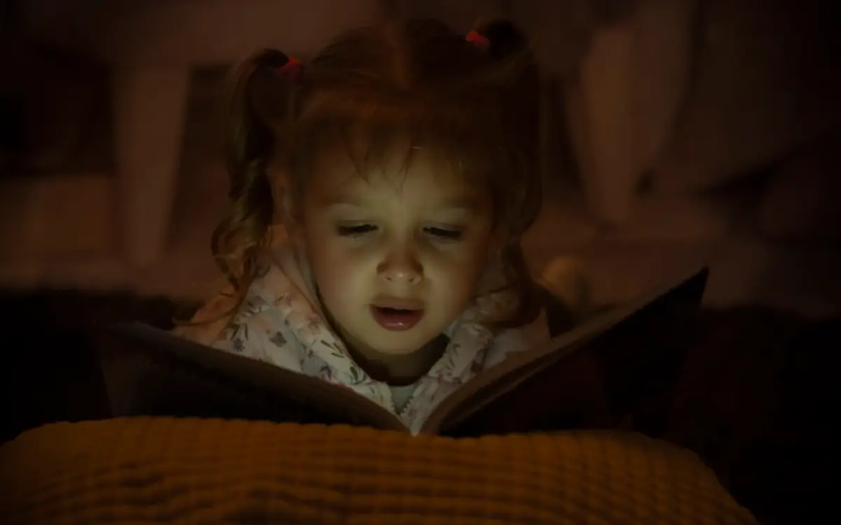 Un enfant lit au calme dans sa chambre, à la lumière d'une lampe, le soir