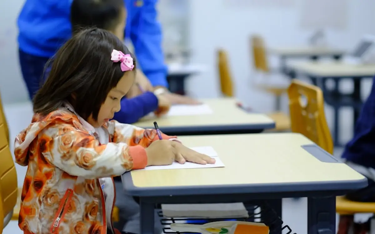 Une enfant écrit à son pupitre en classe, appliquée sur sa feuille